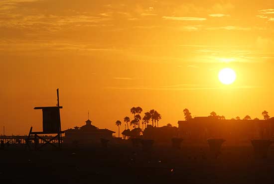 Outline of lifeguard station, palm trees with orange-yellow sunset sky behind
